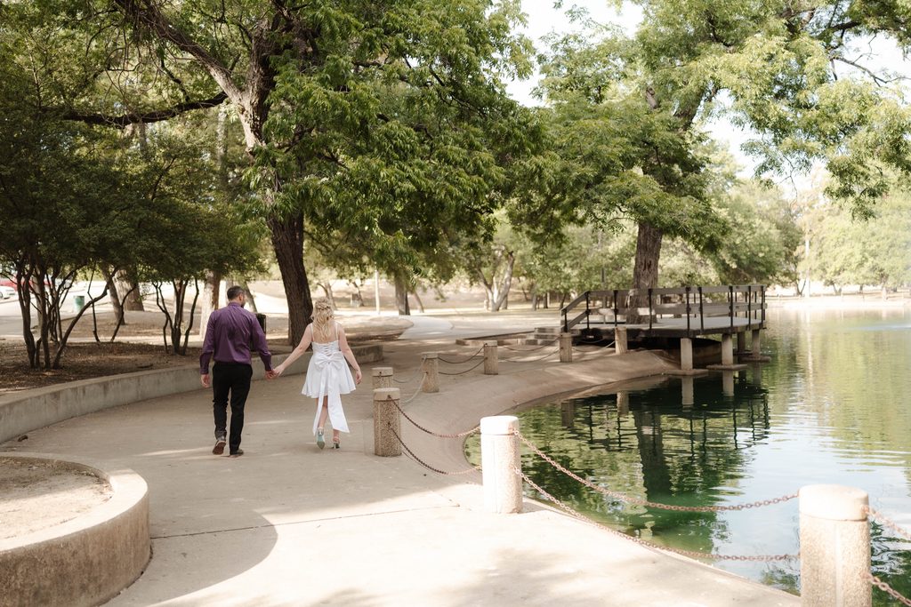 Bride and groom taking wedding portraits and walking in front of the duck pond at Trinity Park in Fort Worth, TX