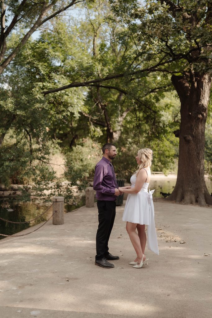 Bride and groom taking wedding portraits in front of the duck pond at Trinity Park in Fort Worth, TX
