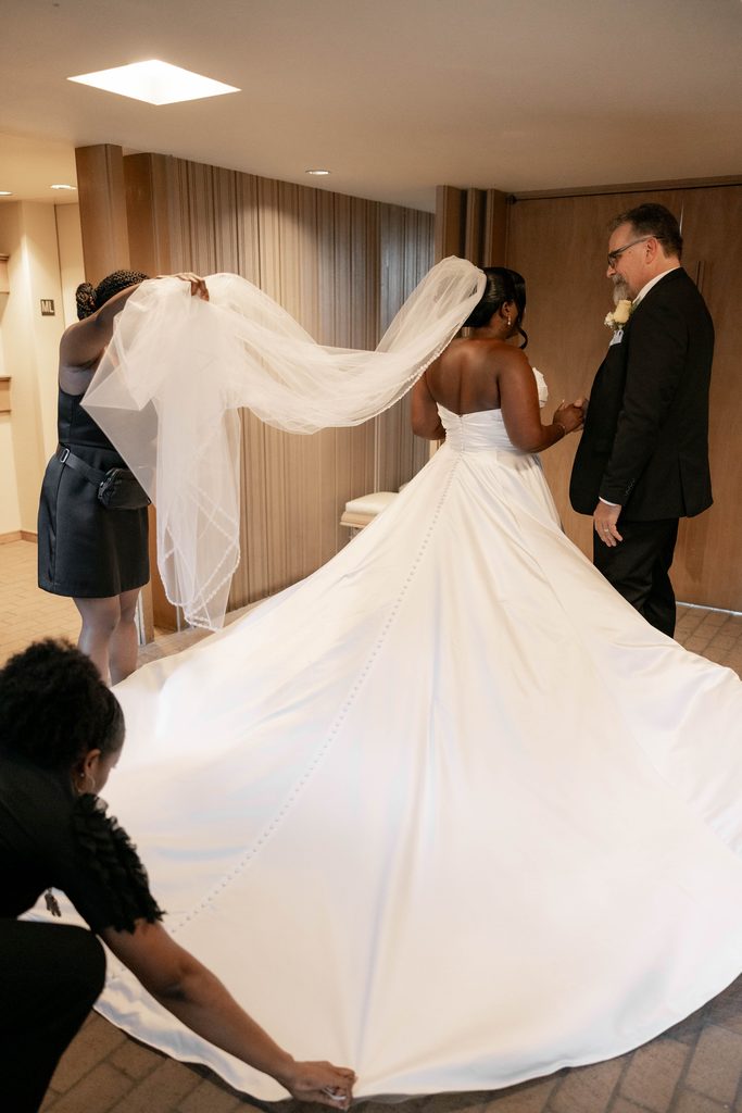 Wedding coordinators fluffing the bride's dress and veil before she walks down the aisle with her father
