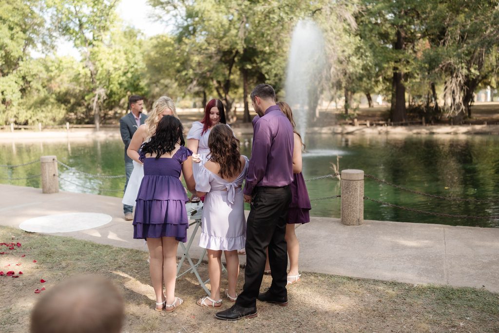 Bride and groom with children in front of the water fountain at the duckpond during their elopement at Trinity Park in Fort Worth, TX