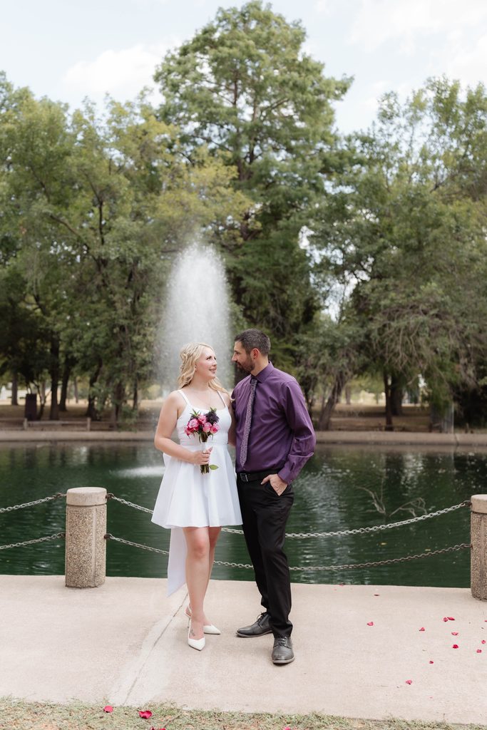 Bride and groom taking wedding portraits and walking along the pathway at the duck pond at Trinity Park in Fort Worth, TX