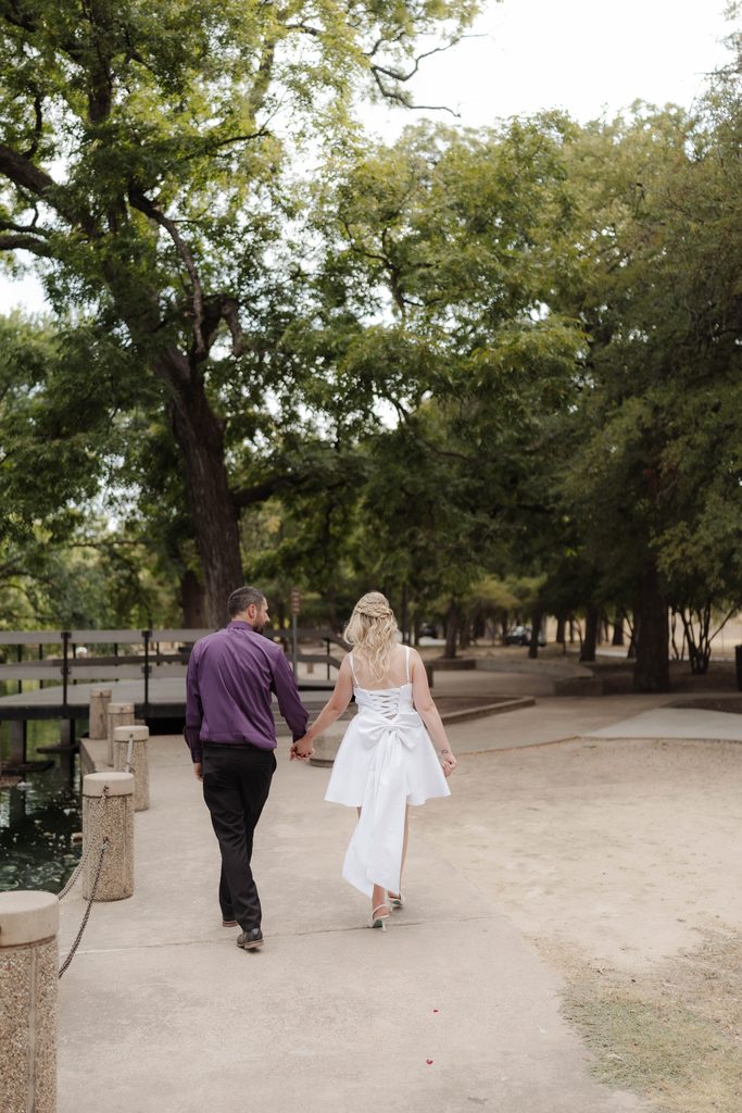Bride and groom taking wedding portraits and walking along the pathway at the duck pond at Trinity Park in Fort Worth, TX