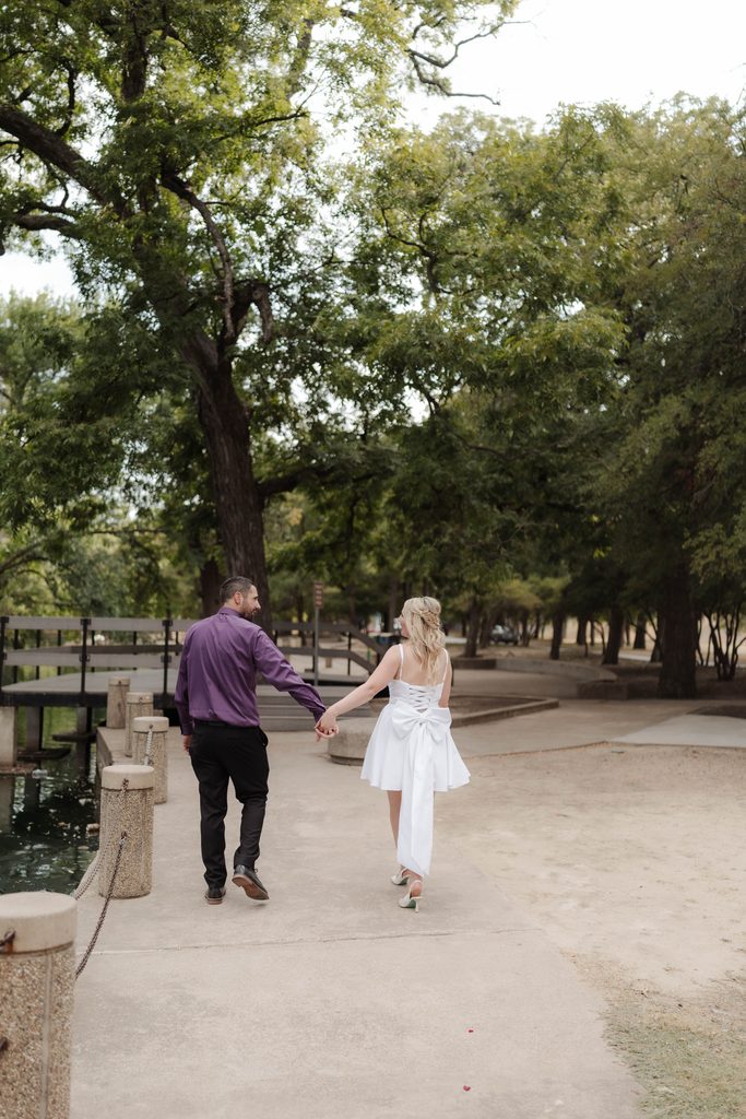 Bride and groom taking wedding portraits and walking along the pathway at the duck pond at Trinity Park in Fort Worth, TX