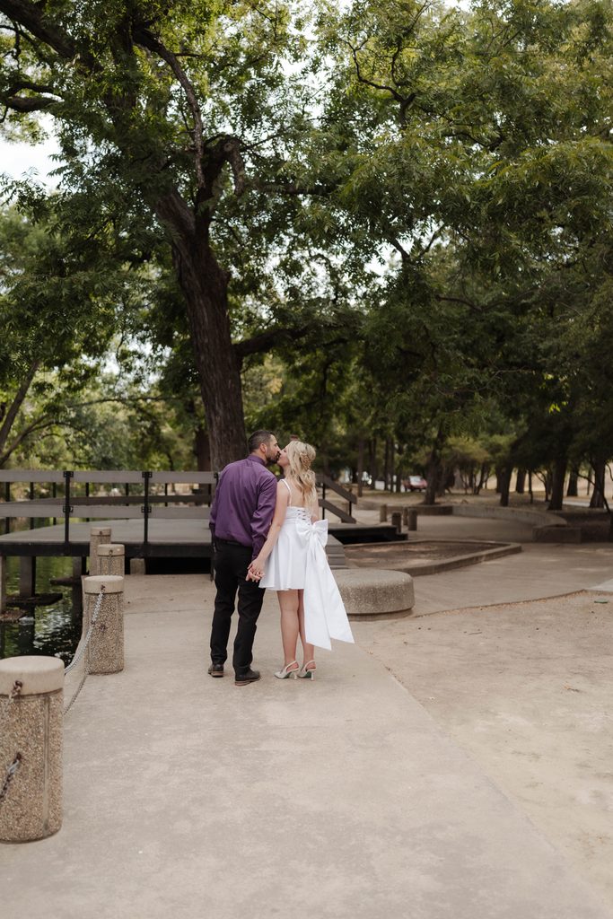 Bride and groom taking wedding portraits and walking along the pathway at the duck pond at Trinity Park in Fort Worth, TX