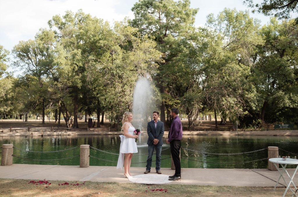 Man and woman exchanging vows in front of the water fountain at the duckpond at Trinity Park in Fort Worth, TX