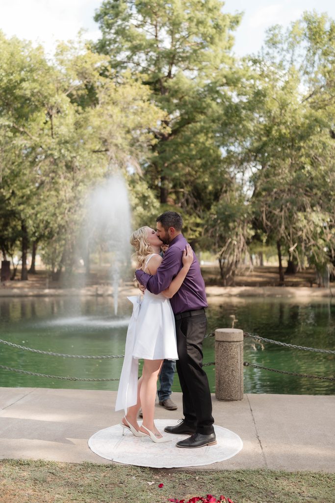 Bride and groom kissing in front of the water fountain at the duckpond during their elopement at Trinity Park in Fort Worth, TX