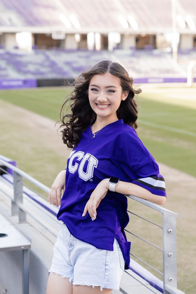 Girl standing on railing during her senior portrait session at the TCU Campus in Fort Worth, TX