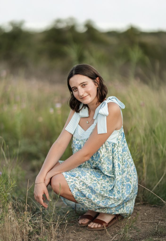 Girl sitting in an open field at Tandy Hills during her golden hour senior portrait session