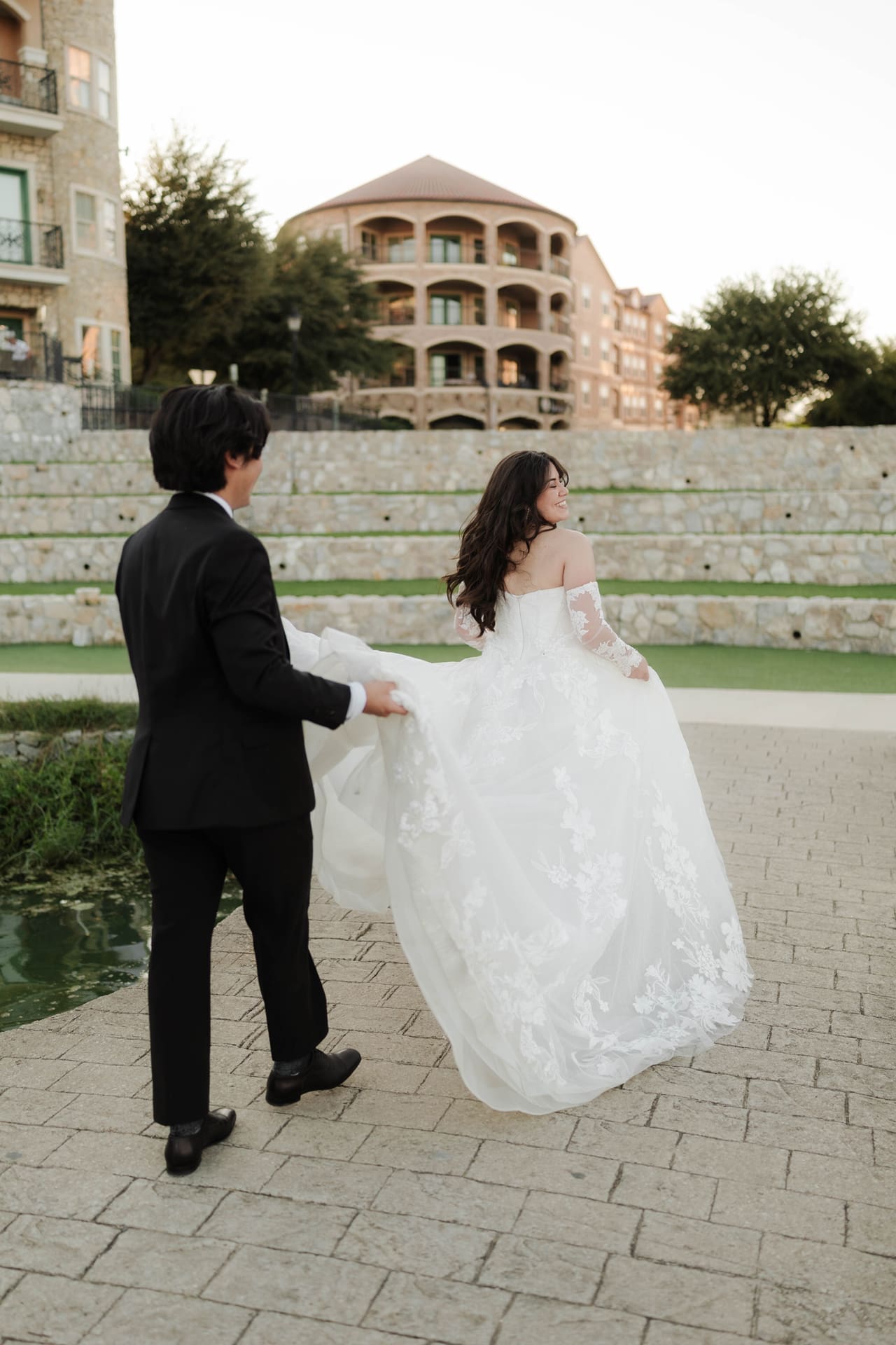 Bride and groom walking across the bridge while the groom holds her dress