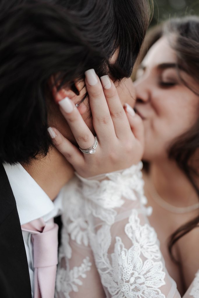 Bride and groom embracing in a kiss with the ring in focus