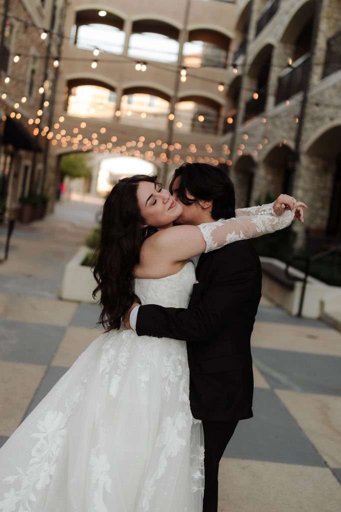 Bride and groom embracing in a kiss under the string lights at Adriatica Village