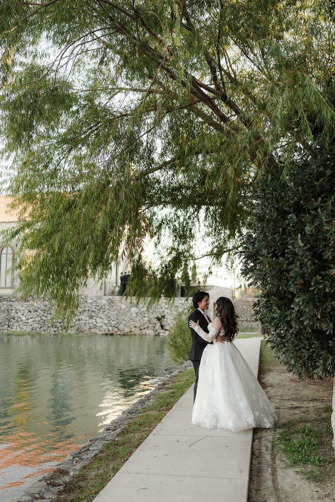 Bride and groom cuddling and walking along the water at Adriatica Village during their portrait session