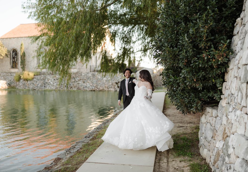 Bride and groom holding hands and walking along the water at Adriatica Village during their portrait session