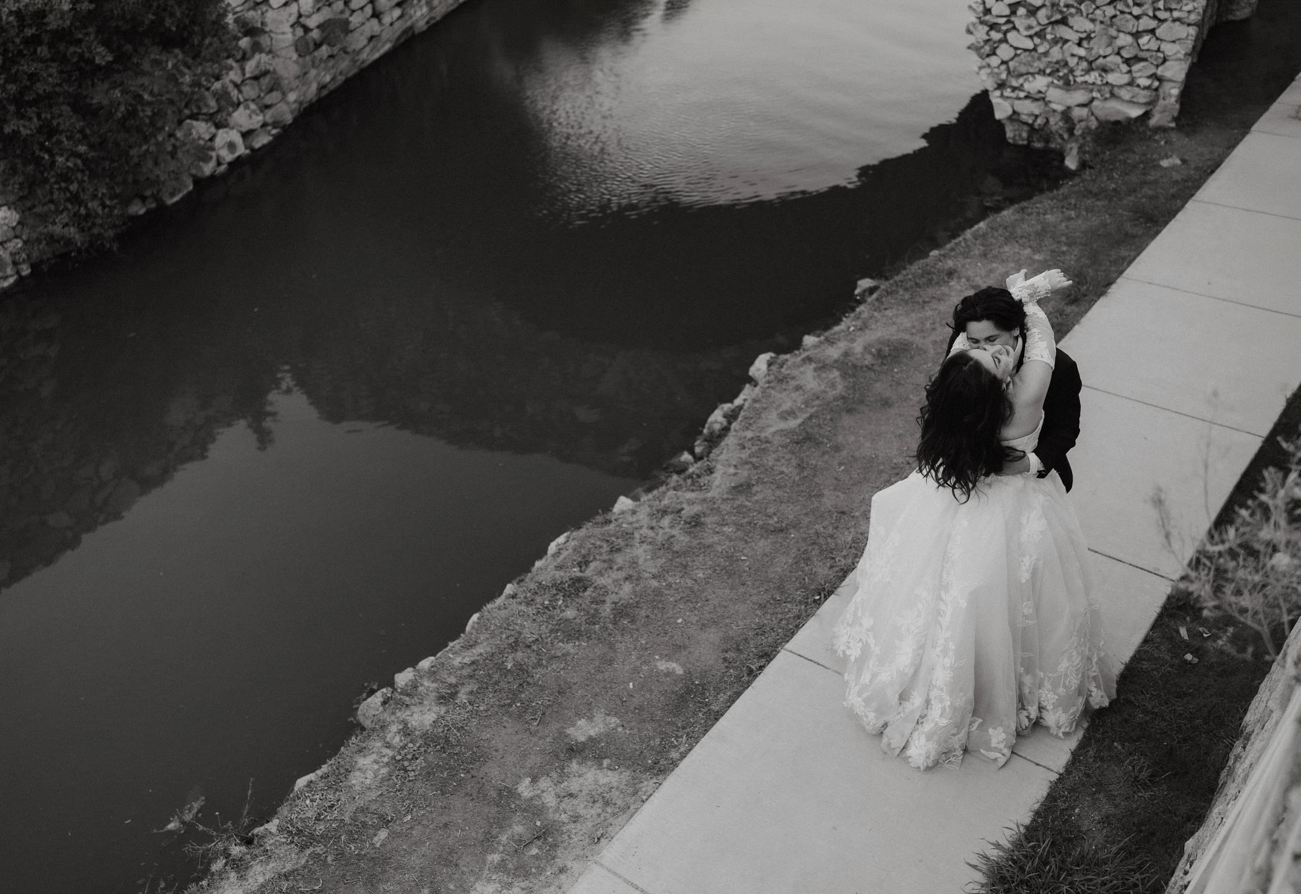 Bride and groom embracing in a kiss along the water's edge at Adriatica Village in McKinney, TX