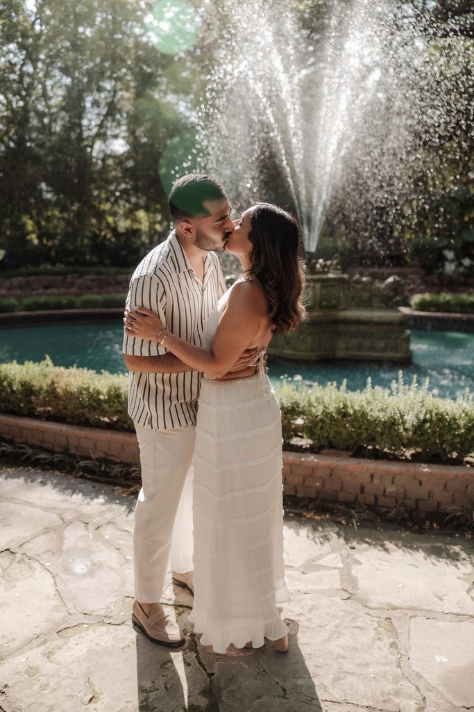 Man and his girlfriend kissing in front of the large fountain in Chandor Gardens, Weatherford, TX during a surprise proposal