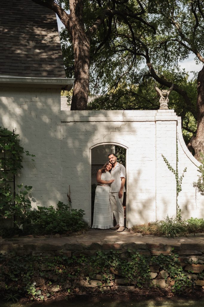 Moody portrait of Man and woman embracing under and archway at Chandor Gardens, Weatherford, TX during their engagement photo session