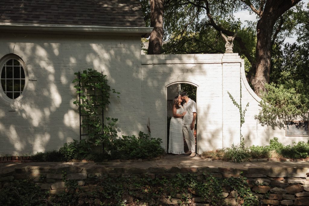 Moody portrait of Man and woman embracing under and archway at Chandor Gardens, Weatherford, TX during their engagement photo session