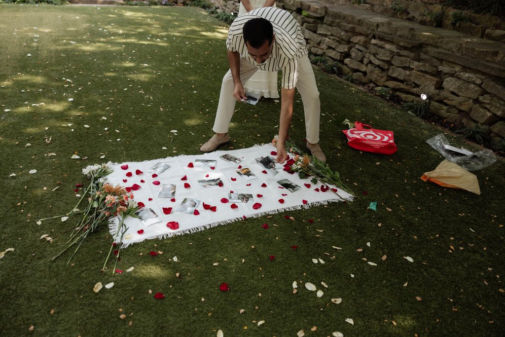 Man laying down a picnic blanket with photos of him and his girlfriend with their cat at Chandor Gardens