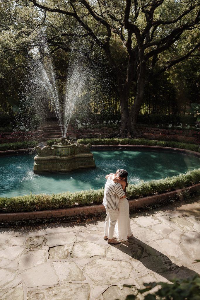 Man and his girlfriend embracing in front of the large fountain in Chandor Gardens, Weatherford, TX during a surprise proposal