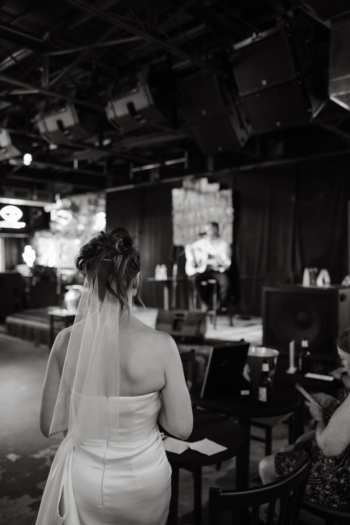 Jason singing and playing guitar on stage at Filthy McNasty's Bar in the Fort Worth Stockyards while his bride watches from a distance