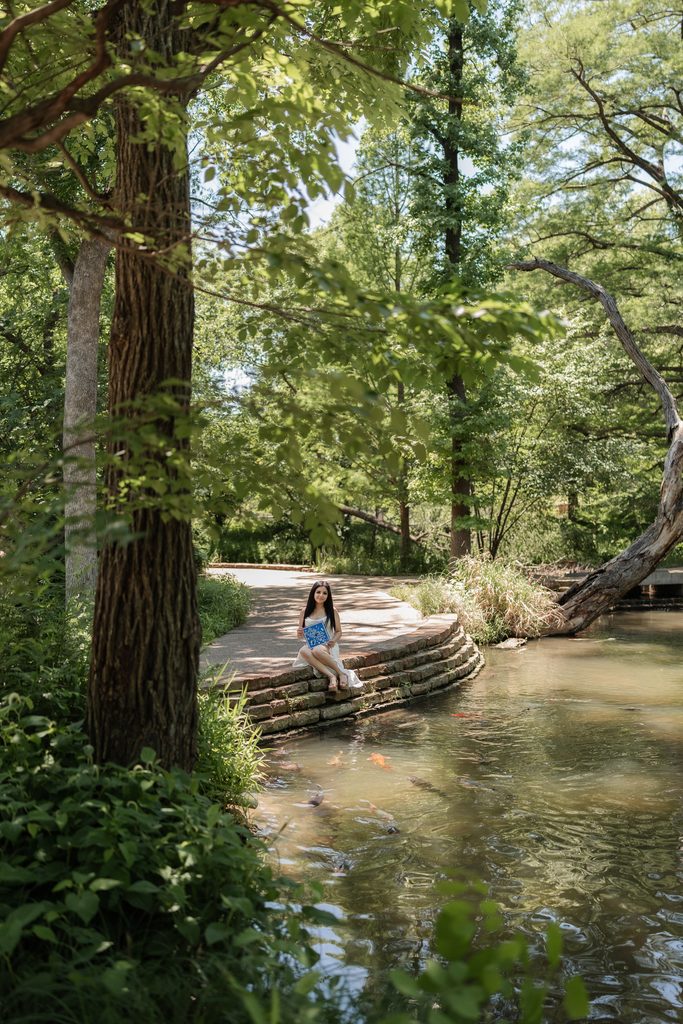 Portrait of girl sitting at the edge of a pond at the Fort Worth Botanic Garden during her senior portrait session