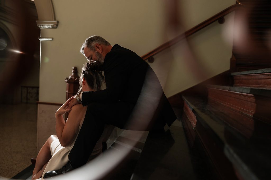 Bride and groom sitting on the steps inside the Tarrant County Courthouse while they take photos during their adventure elopement in Fort Worth