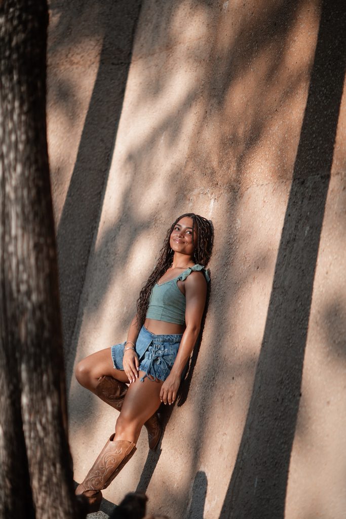 Dramatic lighting portrait of girl posing against a wall at the Fort Worth Water Gardens during her senior portrait session