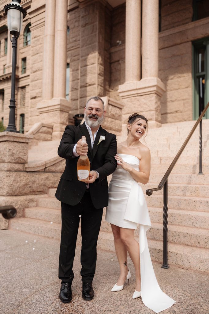 Bride + Groom popping champagne on the steps of the Fort Worth Courthouse 