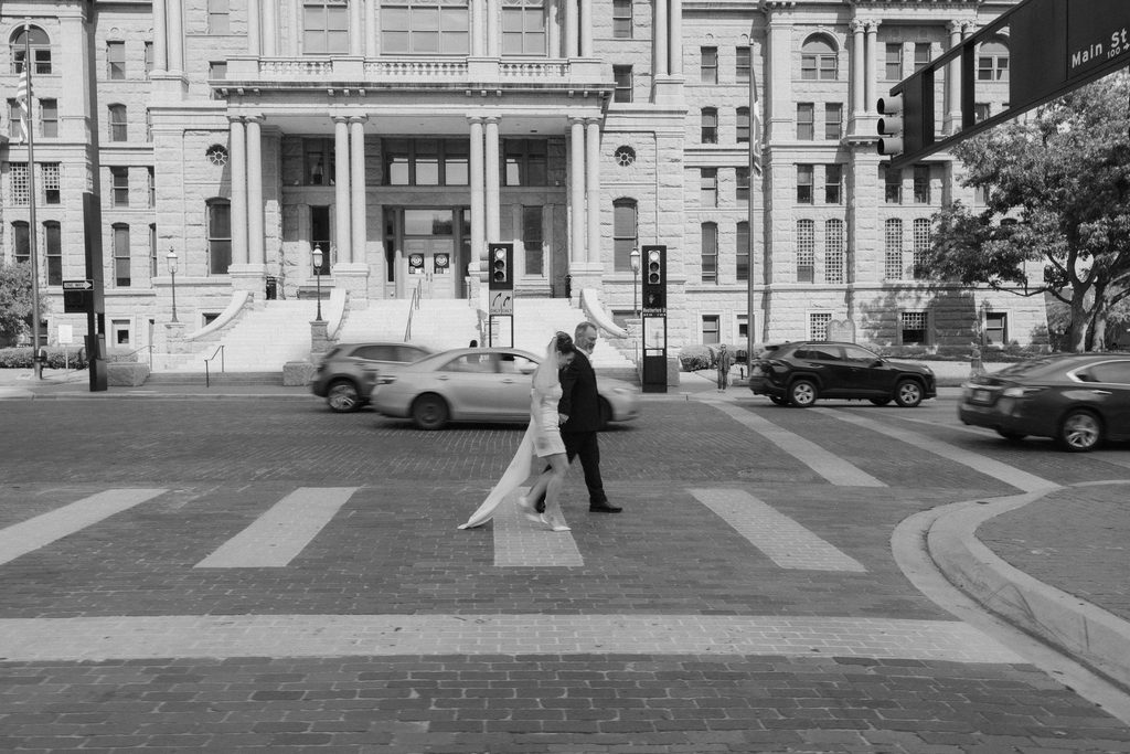Bride + Groom walking across the street in front of the Fort Worth Courthouse