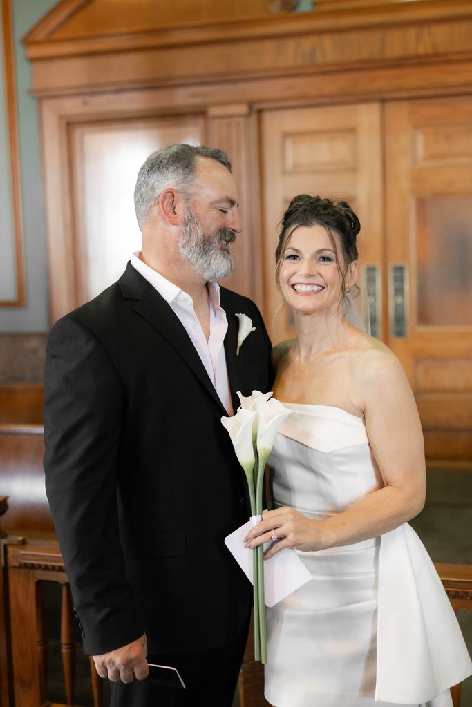Bride + Groom smiling in the courtroom at the Tarrant County Courthouse during their adventure elopement in Fort Worth